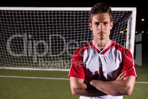 Confident male soccer player standing with arms crossed against goal post on field