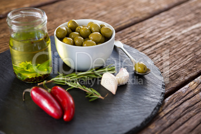 Green olives, fresh herbs with olive oil and red chilies on table