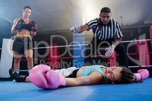 Female boxer looking while referee counting by athlete
