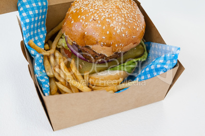 Hamburger and french fries in a take away container on table