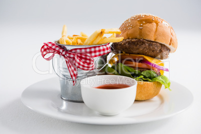 Hamburger by french fries in container with tomato sauce