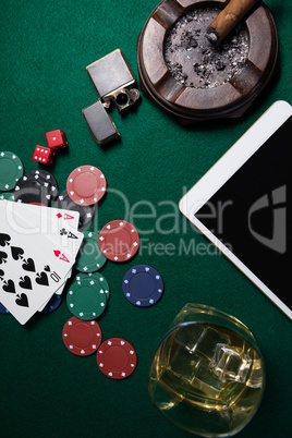 Ashtray, lighter, digital tablet, dice, casino chips and playing cards on poker table