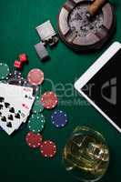 Ashtray, lighter, digital tablet, dice, casino chips and playing cards on poker table