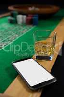 Close-up of mobile phone and whisky glass on roulette table