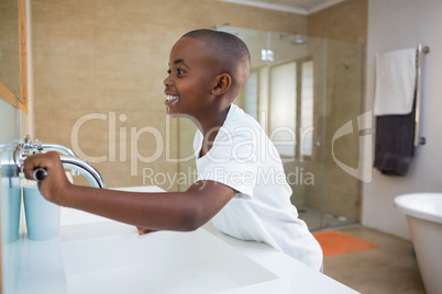 Side view of smiling boy with toothbrush looking at mirror