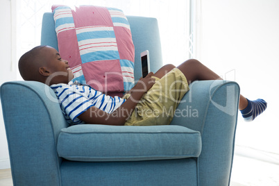 Side view of smiling boy looking at mobile phone while lying on armchair