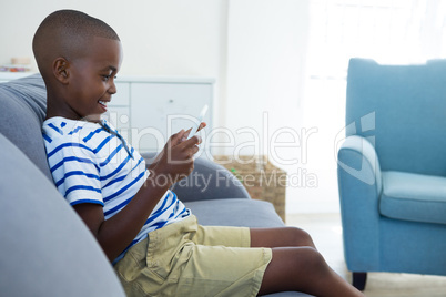 Side view of smiling boy using mobile phone while sitting on sofa at home