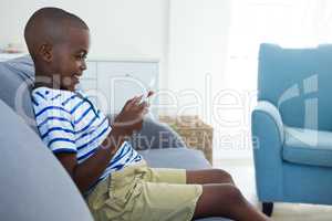 Side view of smiling boy using mobile phone while sitting on sofa at home