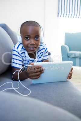 Portrait of boy using digital tablet while listening to headphones on sofa at home