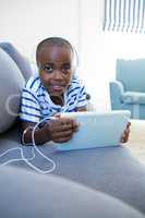 Portrait of boy using digital tablet while listening to headphones on sofa at home