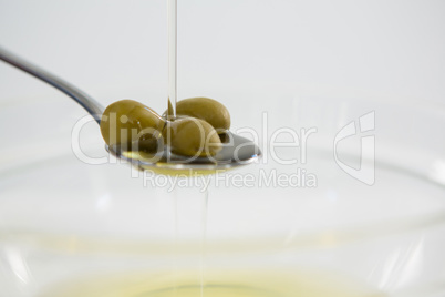Green olive oil being poured in spoon