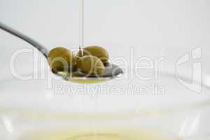 Green olive oil being poured in spoon