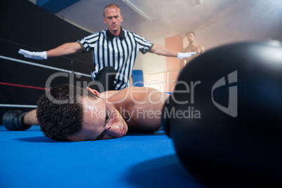 Referee gesturing with arms outstretched by unconscious male boxer
