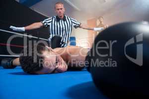 Referee gesturing with arms outstretched by unconscious male boxer