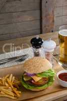 Hamburger, french fries, tomato sauce and glass of beer on chopping board