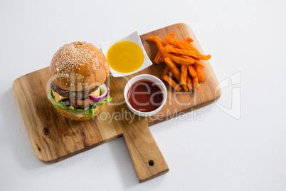 Close up dips with French fries and burger on cutting board