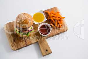 Close up dips with French fries and burger on cutting board