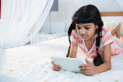 Girl using tablet while lying on bed at home