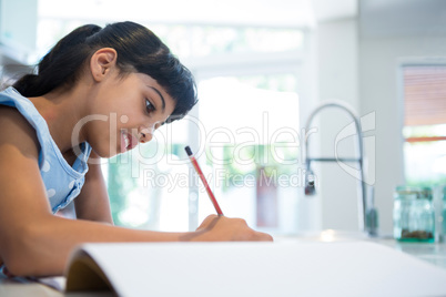 Side view of girl writing in book against window