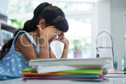 Side view of exhausted girl sitting by books in kitchen