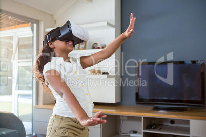 Smiling girl using virtual reality simulator while standing in living room