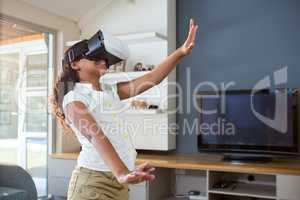 Smiling girl using virtual reality simulator while standing in living room
