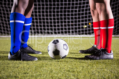 Low section of male players standing by soccer ball against goal post
