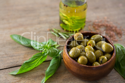 Marinated green olives in bowl and oil container with green leaf on table