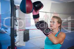 Young female boxer punching bag by boxing ring