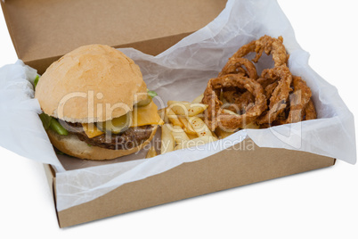 Hamburger, onion ring and french fries in a take away container on table
