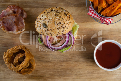 Hamburger, french fries, onion ring and tomato sauce on chopping board