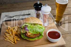 Hamburger, french fries, tomato sauce and glass of beer on chopping board