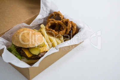 Close up of burger with onion rings and French fries in box