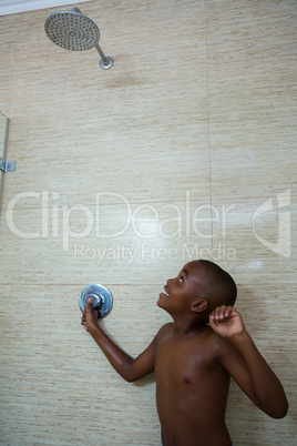 Smiling shirtless boy looking at shower head