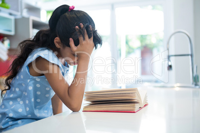 Girl with hand in hair reading novel in kitchen