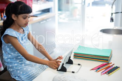 High angle view of girl using digital tablet by colored pencils on kitchen counter