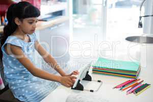 High angle view of girl using digital tablet by colored pencils on kitchen counter