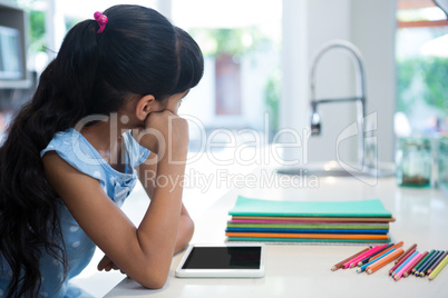 Girl looking away while sitting with tablet and colored pencils