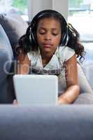 Girl using tablet computer while lying on sofa