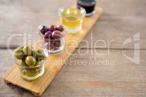 Marinated olives with olive oil and balsamic vinegar in glass container on a wooden tray