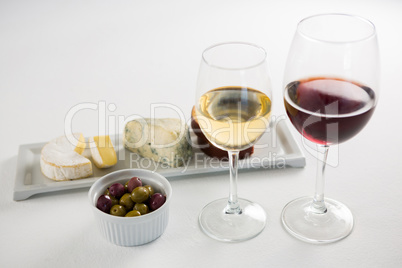 Close-up marinated olives with glasses of wine and cheese in tray