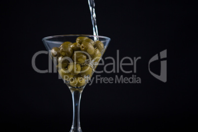 Martini pouring into glass with olives