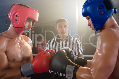 Referee looking at male boxers punching gloves
