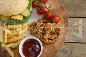 Hamburger, onion ring, tomato sauce, cherry tomato and french fries on chopping board