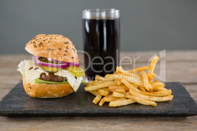 Cheeseburger with french fries and drink on slate