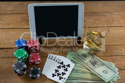 High angle view of digital tablet and whisky with currency on table during poker game