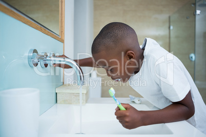 Side view of boy spitting while holding brush in sink