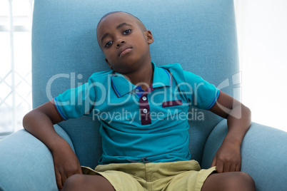 Portrait of boy sitting on blue armchair at home