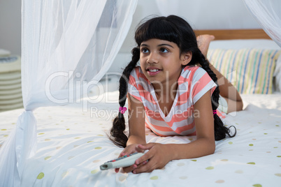 Girl holding remote control while lying on bed