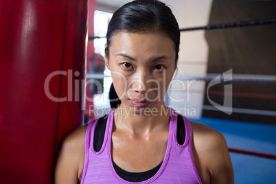 Close-up portrait of confident young female athlete against boxing ring